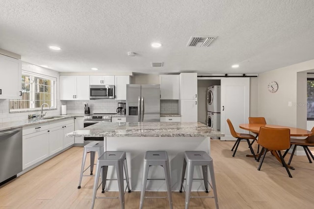 201 S St, Palm Harbor, FL 34683 - kitchen featuring stainless steel appliances, stacked washer and clothes dryer, a textured ceiling, a kitchen breakfast bar, and light wood-style flooring
