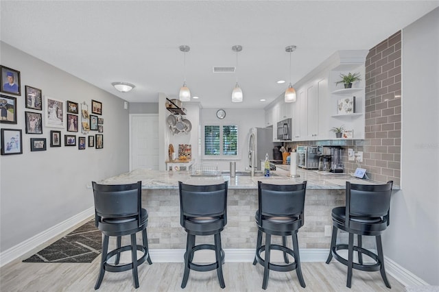900 Maclaren Dr N Unit D, Palm Harbor, FL 34684 - kitchen with stainless steel appliances, open shelves, a peninsula, white cabinetry, and light wood-style floors