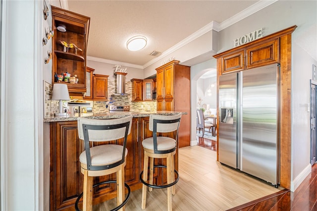 1205 Sweet Gum Dr, Brandon, FL 33511 - kitchen with stainless steel appliances, arched walkways, wall chimney range hood, light stone counters, and tasteful backsplash