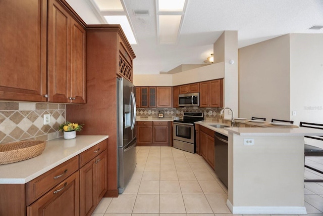 12405 Pathway Ct, Riverview, FL 33569 - kitchen with stainless steel appliances, a peninsula, light tile patterned floors, brown cabinetry, and decorative backsplash