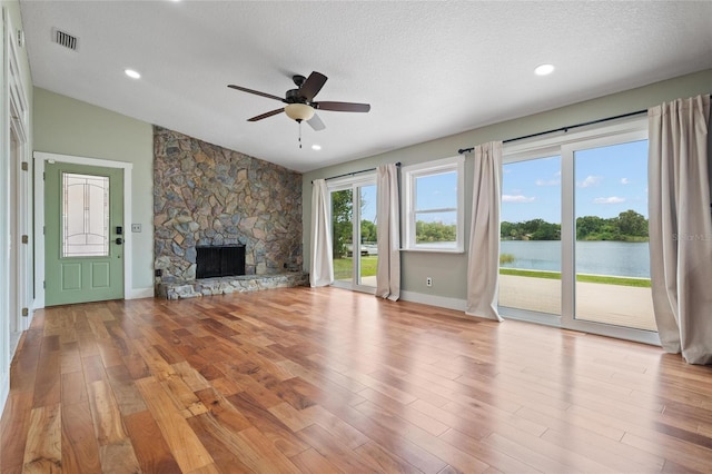17 Freshwater Dr, Palm Harbor, FL 34684 - unfurnished living room with a water view, ceiling fan, a stone fireplace, wood finished floors, and a textured ceiling
