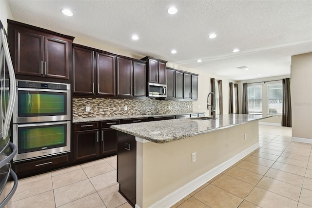 4544 Vermillion Sky Dr, Wesley Chapel, FL 33544 - kitchen with stainless steel appliances, light tile patterned flooring, backsplash, an island with sink, and a textured ceiling