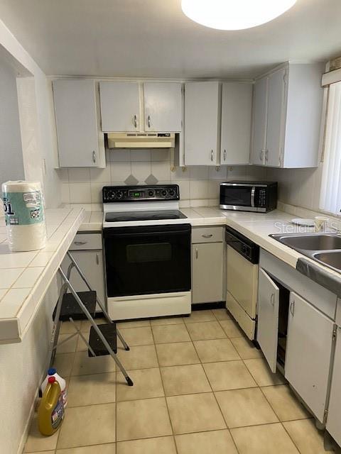 8636 Tahoe Ct Unit 13, Tampa, FL 33614 - kitchen with range with electric stovetop, stainless steel microwave, dishwashing machine, under cabinet range hood, and tile countertops