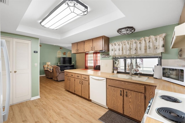 7022 Kingsway Dr, Port Richey, FL 34668 - kitchen featuring white appliances, a tray ceiling, light wood-type flooring, light countertops, and brown cabinetry