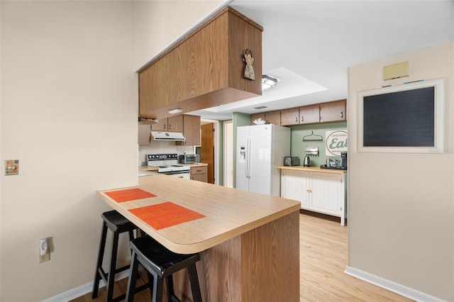 7022 Kingsway Dr, Port Richey, FL 34668 - kitchen with white appliances, a peninsula, light countertops, a breakfast bar area, and under cabinet range hood
