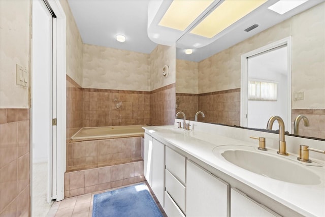 17025 Dolphin Dr, North Redington Beach, FL 33708 - bathroom featuring tile walls, double vanity, a relaxing tiled tub, tile patterned flooring, and wainscoting