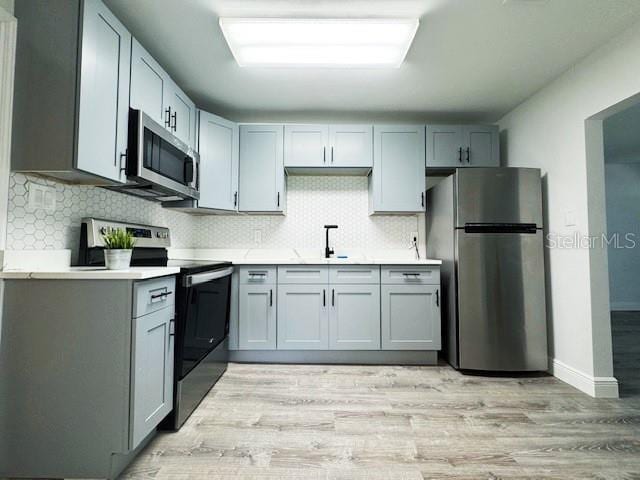 1400 E Fern Rd, Lakeland, FL 33801 - kitchen with appliances with stainless steel finishes, light countertops, decorative backsplash, light wood-type flooring, and gray cabinetry