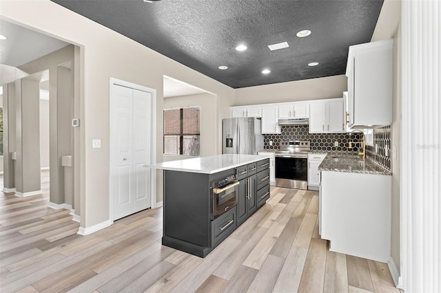 1291 Blackrush Dr, Tarpon Springs, FL 34689 - kitchen featuring stainless steel appliances, under cabinet range hood, white cabinets, light wood-style floors, and a kitchen island