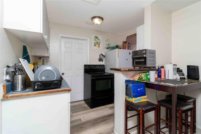 1144AND1142 7th St NW, Largo, FL 33770 - kitchen featuring black electric range oven, wood finished floors, stainless steel microwave, and white cabinets