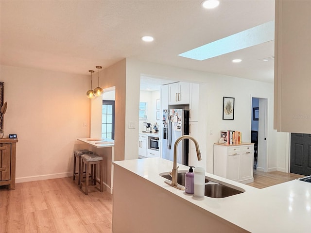 1972 Briarwood St, Dunedin, FL 34698 - kitchen with appliances with stainless steel finishes, light wood-style flooring, white cabinetry, a skylight, and pendant lighting