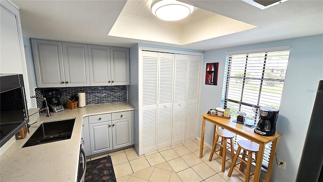 13 Windrush Bay Dr, Tarpon Springs, FL 34689 - kitchen with gray cabinets, a tray ceiling, light tile patterned flooring, and decorative backsplash