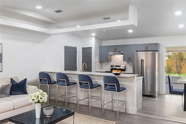 22716 Penny Loop, Land O Lakes, FL 34639 - kitchen featuring stainless steel appliances, under cabinet range hood, vaulted ceiling, a kitchen bar, and tasteful backsplash