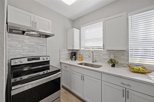 1048 W Lime St, Lakeland, FL 33815 - kitchen with stainless steel electric range, under cabinet range hood, white cabinetry, a textured ceiling, and decorative backsplash