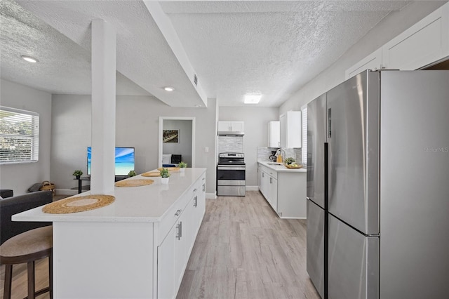 1048 W Lime St, Lakeland, FL 33815 - kitchen featuring stainless steel appliances, a textured ceiling, light wood finished floors, white cabinetry, and a breakfast bar area