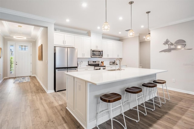 6879 Talamore Dr, Wesley Chapel, FL 33545 - kitchen featuring appliances with stainless steel finishes, a center island with sink, light wood-style flooring, white cabinets, and crown molding