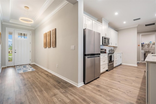 6879 Talamore Dr, Wesley Chapel, FL 33545 - kitchen with stainless steel appliances, light wood-style floors, ornamental molding, white cabinets, and washing machine and dryer