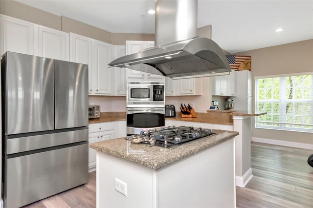 6513 Sand Shore Ln, New Port Richey, FL 34652 - kitchen with appliances with stainless steel finishes, island exhaust hood, white cabinetry, light wood-type flooring, and a center island