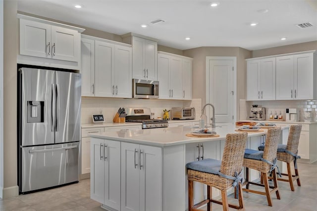 5320 Morey Farms Loop, Palmetto, FL 34221 - kitchen with appliances with stainless steel finishes, tasteful backsplash, white cabinets, an island with sink, and light countertops