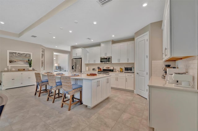 5320 Morey Farms Loop, Palmetto, FL 34221 - kitchen featuring stainless steel appliances, a center island with sink, tasteful backsplash, a kitchen breakfast bar, and white cabinetry