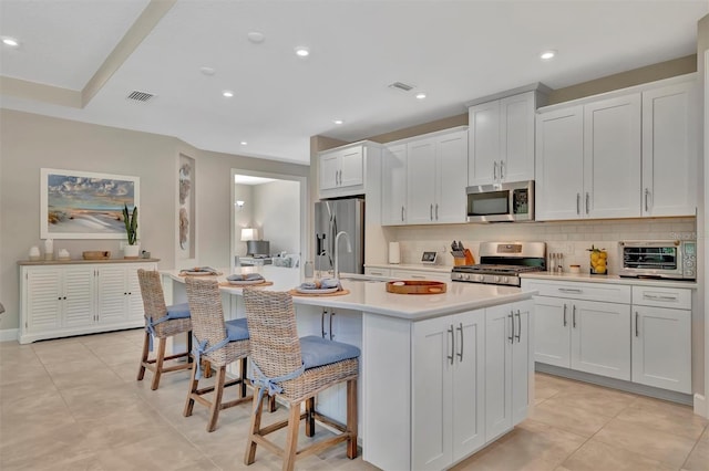 5320 Morey Farms Loop, Palmetto, FL 34221 - kitchen featuring stainless steel appliances, a kitchen island with sink, a breakfast bar, decorative backsplash, and light countertops