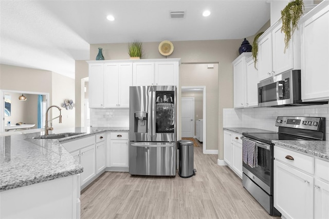 12333 Harris Hawk Rd, Weeki Wachee, FL 34614 - kitchen featuring stainless steel appliances, white cabinets, light wood-style flooring, a peninsula, and tasteful backsplash