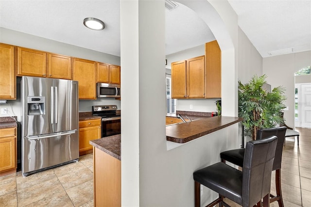 19028 Narimore Dr, Land O Lakes, FL 34638 - kitchen with stainless steel appliances, dark countertops, a breakfast bar area, arched walkways, and a peninsula