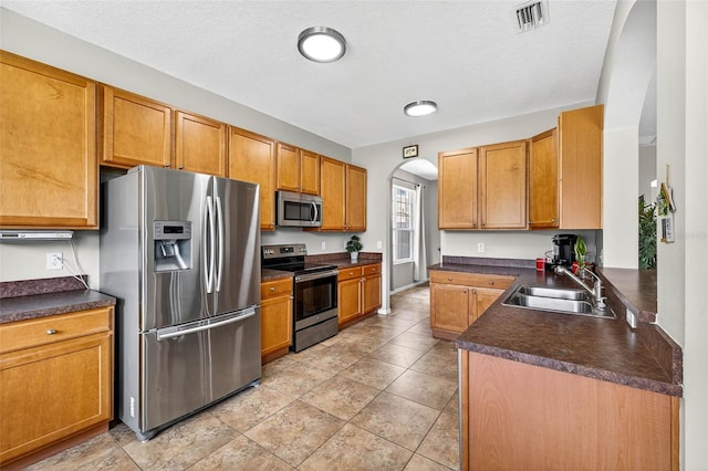 19028 Narimore Dr, Land O Lakes, FL 34638 - kitchen with appliances with stainless steel finishes, arched walkways, dark countertops, brown cabinetry, and a textured ceiling