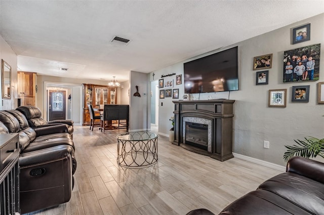 1403 Tallahassee Dr, Tarpon Springs, FL 34689 - living room featuring light wood-style flooring, a glass covered fireplace, a chandelier, and a textured ceiling