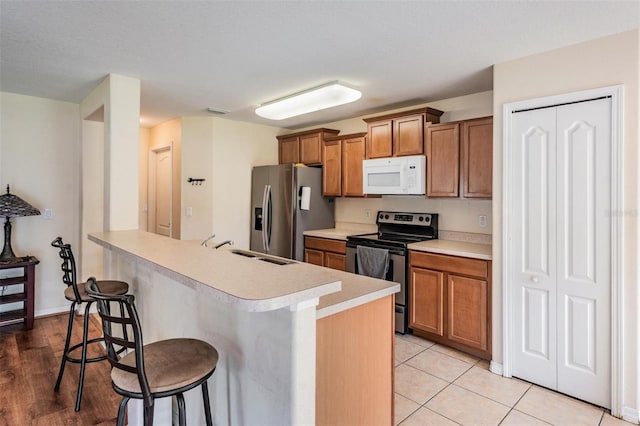 15420 Quail Woods Pl, Ruskin, FL 33573 - kitchen with stainless steel appliances, a kitchen breakfast bar, brown cabinets, light countertops, and a peninsula