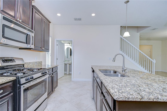 828 Terra Vista St, Brandon, FL 33511 - kitchen featuring stainless steel appliances, a kitchen island with sink, dark brown cabinetry, hanging light fixtures, and light stone counters