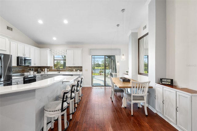 12830 24th Street Cir E, Parrish, FL 34219 - kitchen with stainless steel appliances, a kitchen breakfast bar, backsplash, dark wood-type flooring, and white cabinetry