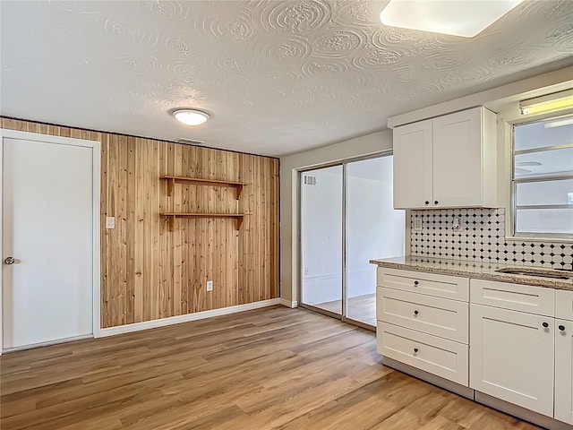 6632 Sierra Ter, New Port Richey, FL 34652 - kitchen with white cabinets, wooden walls, light wood-style floors, backsplash, and light stone countertops