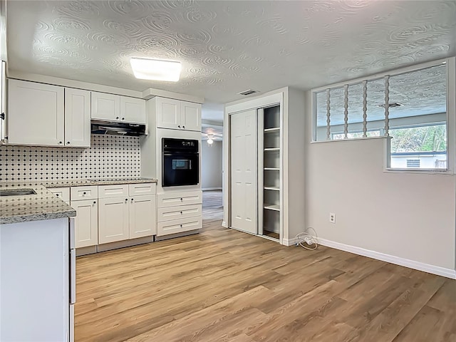 6632 Sierra Ter, New Port Richey, FL 34652 - kitchen with black oven, under cabinet range hood, white cabinets, light wood-style flooring, and light stone counters