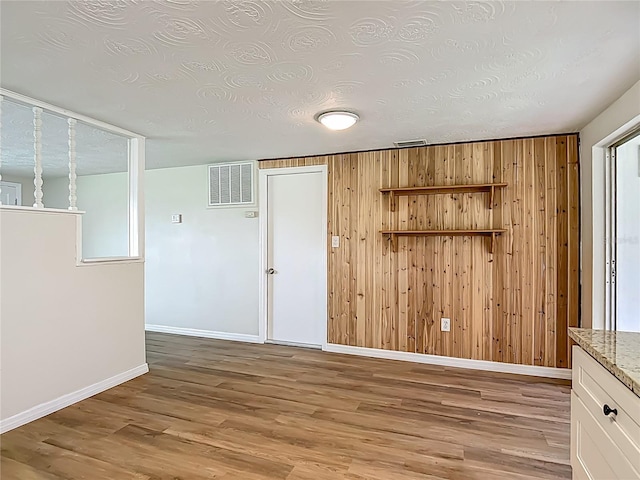 6632 Sierra Ter, New Port Richey, FL 34652 - spare room with wood walls, light wood-style flooring, and a textured ceiling