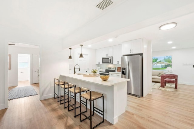 11779 82nd Ter, Seminole, FL 33772 - kitchen with appliances with stainless steel finishes, a breakfast bar, white cabinetry, light wood-style floors, and a peninsula