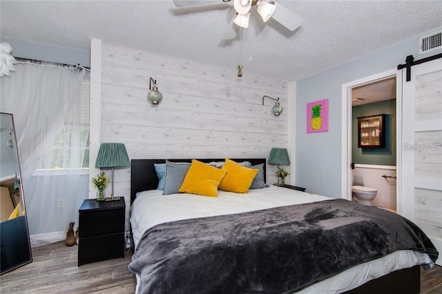 6932 Stones Throw Cir N Unit 7101, Saint Petersburg, FL 33710 - bedroom featuring wood finished floors, a textured ceiling, wood walls, a barn door, and ensuite bath