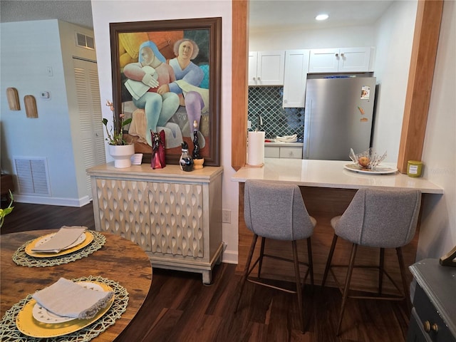 5925 Terrace Park Dr N Unit 210, Saint Petersburg, FL 33709 - kitchen featuring freestanding refrigerator, dark wood-style flooring, a breakfast bar, white cabinetry, and backsplash