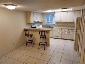 14442 Reuter Strasse Cir Unit 812, Tampa, FL 33613 - kitchen featuring stove, a peninsula, a kitchen bar, white cabinets, and light countertops