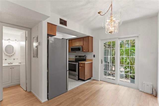 441 75th Ave N, Saint Petersburg, FL 33702 - kitchen featuring appliances with stainless steel finishes, light wood-type flooring, brown cabinetry, a textured ceiling, and backsplash