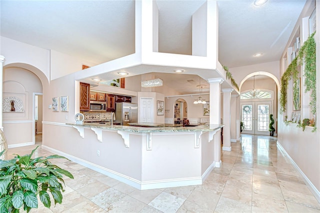 19307 Wind Dancer St, Lutz, FL 33558 - kitchen featuring brown cabinets, arched walkways, french doors, a kitchen breakfast bar, and a peninsula