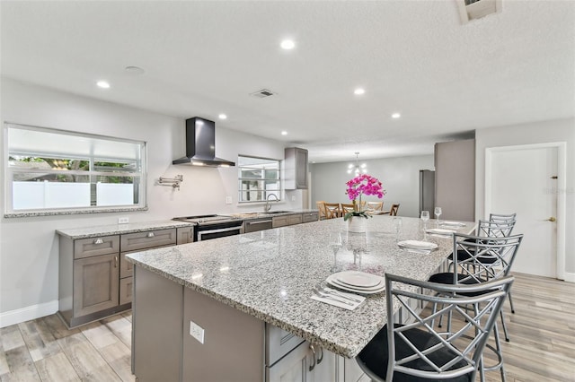 446 Eagle Cir, Casselberry, FL 32707 - kitchen featuring wall chimney range hood, appliances with stainless steel finishes, light wood finished floors, a spacious island, and light stone countertops