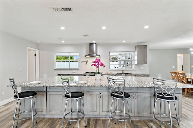 446 Eagle Cir, Casselberry, FL 32707 - kitchen with gray cabinets, wall chimney exhaust hood, a large island with sink, light wood finished floors, and recessed lighting