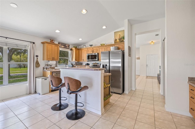 11830 Autumn Creek Dr, Riverview, FL 33569 - kitchen with appliances with stainless steel finishes, a center island, vaulted ceiling, light tile patterned flooring, and a kitchen bar