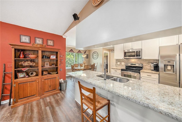 6709 Peachtree Dr, Temple Terrace, FL 33617 - kitchen featuring appliances with stainless steel finishes, wood finished floors, a kitchen breakfast bar, white cabinetry, and light stone counters