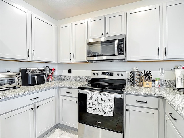 34033 Jasper Stone Dr, Wesley Chapel, FL 33543 - kitchen with stainless steel appliances, light stone counters, light tile patterned flooring, and white cabinets