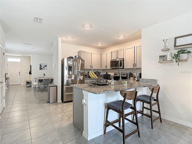 34033 Jasper Stone Dr, Wesley Chapel, FL 33543 - kitchen featuring appliances with stainless steel finishes, a peninsula, a breakfast bar, stone counters, and light tile patterned floors