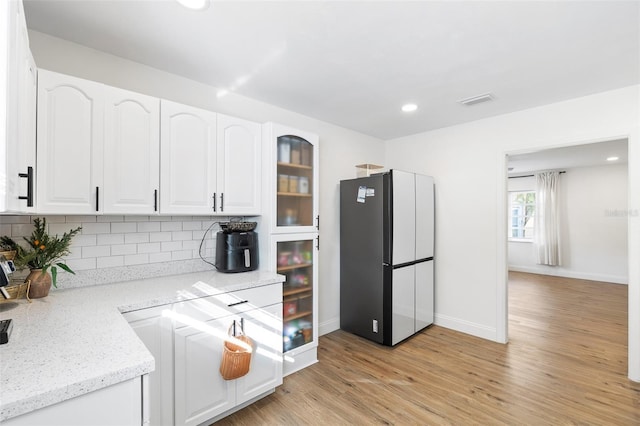 5055 9th St, Zephyrhills, FL 33542 - kitchen with freestanding refrigerator, white cabinetry, decorative backsplash, light wood-style floors, and glass insert cabinets