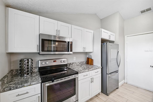 602 Timber Bay Cir W, Oldsmar, FL 34677 - kitchen featuring appliances with stainless steel finishes, light wood finished floors, lofted ceiling, white cabinets, and dark stone counters
