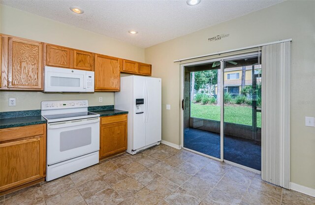 1241 Redondo Way, Wesley Chapel, FL 33543 - kitchen with white appliances, dark countertops, a textured ceiling, brown cabinetry, and recessed lighting