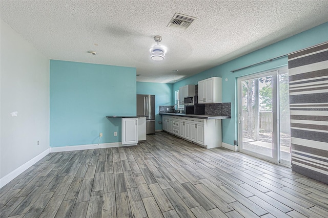 739 Chesapeake Dr, Tarpon Springs, FL 34689 - kitchen featuring light wood finished floors, appliances with stainless steel finishes, white cabinetry, dark countertops, and a textured ceiling